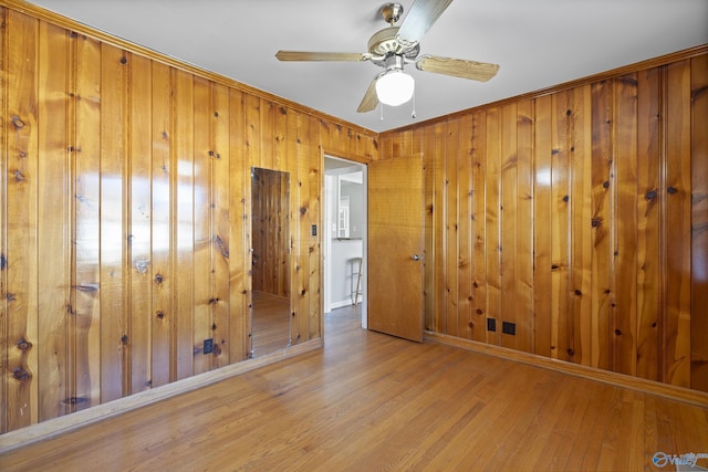 empty room with a ceiling fan, wood finished floors, baseboards, and wood walls