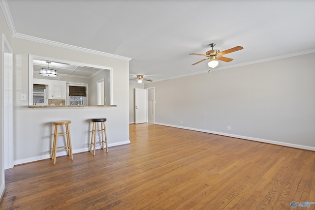 unfurnished living room with a ceiling fan, crown molding, wood finished floors, and baseboards