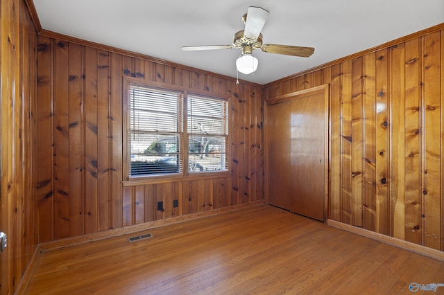 interior space featuring baseboards, visible vents, light wood-style flooring, ceiling fan, and wood walls