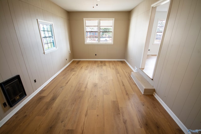 unfurnished room featuring wood walls, heating unit, and light wood-type flooring