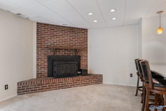 carpeted living room with a drop ceiling, a brick fireplace, and brick wall