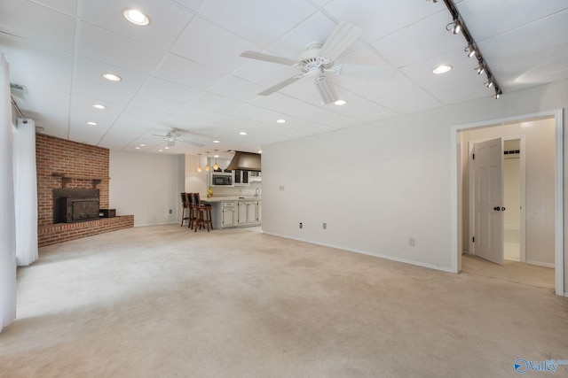 unfurnished living room with ceiling fan, rail lighting, brick wall, light colored carpet, and a brick fireplace