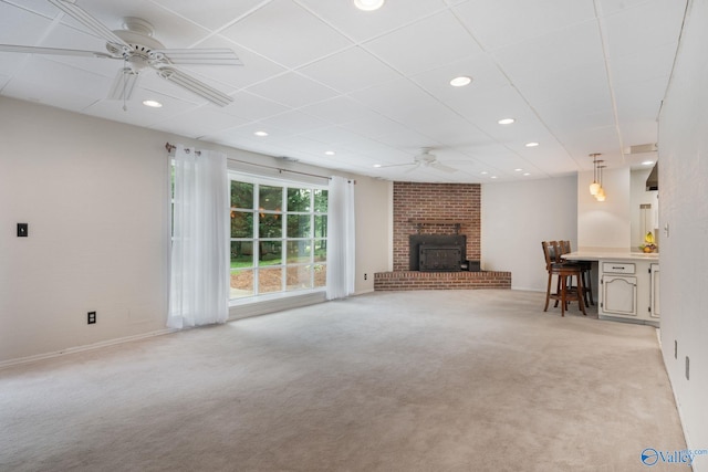 unfurnished living room featuring ceiling fan, brick wall, a brick fireplace, and light colored carpet