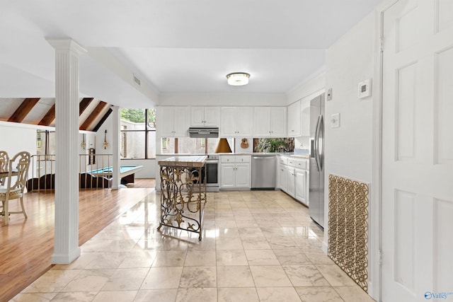 102 Fern Cv, Florence, AL 35634 - kitchen featuring stainless steel appliances, under cabinet range hood, light countertops, white cabinetry, and decorative columns