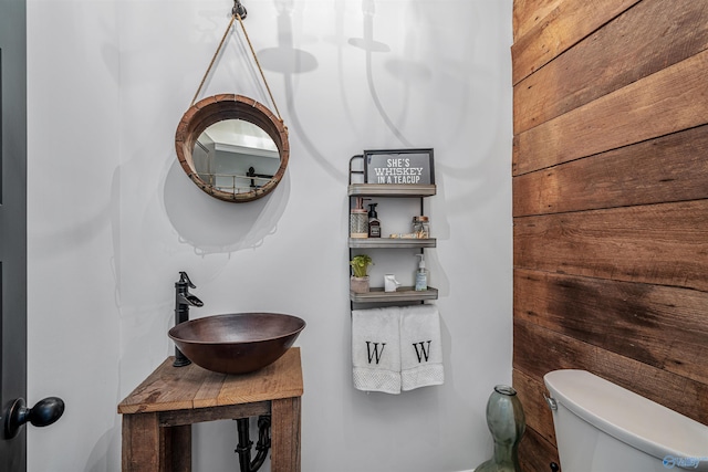 bathroom featuring sink, wooden walls, and toilet