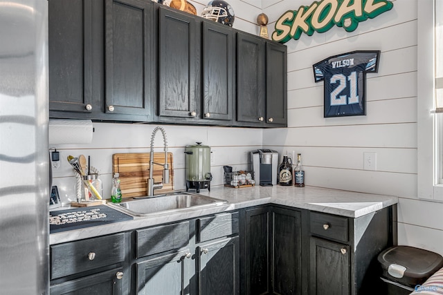 kitchen featuring sink, wooden walls, and stainless steel refrigerator