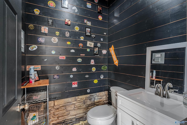 bathroom with vanity, toilet, and wood walls