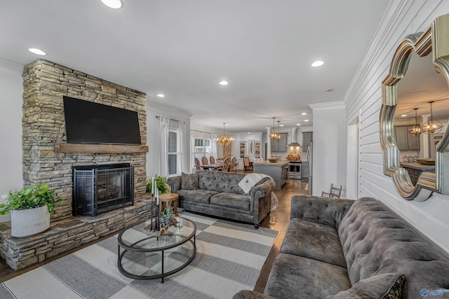 living room featuring hardwood / wood-style flooring, crown molding, a stone fireplace, and an inviting chandelier