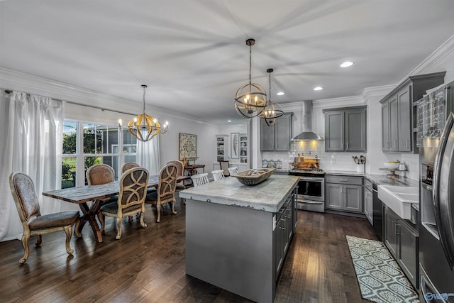 kitchen with wall chimney range hood, gray cabinets, stainless steel appliances, a kitchen island, and decorative light fixtures