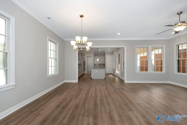 unfurnished living room featuring crown molding, plenty of natural light, dark wood-type flooring, and ceiling fan with notable chandelier