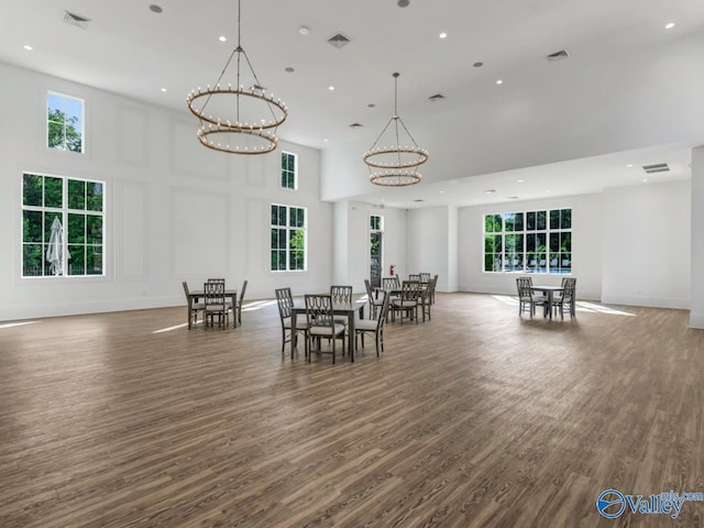 dining area with dark wood-type flooring, a notable chandelier, and a towering ceiling