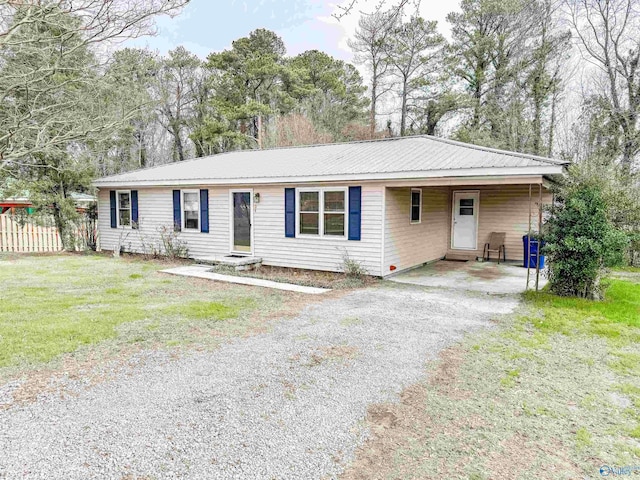 ranch-style house with gravel driveway, metal roof, fence, and a front lawn