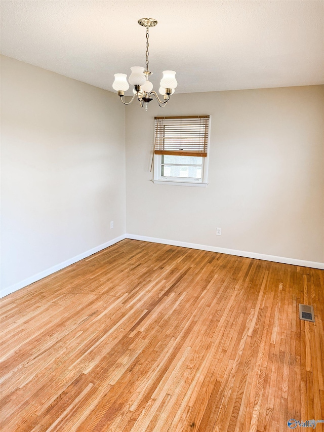 empty room with wood finished floors, visible vents, baseboards, and an inviting chandelier