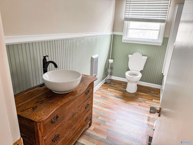 half bath featuring visible vents, toilet, a wainscoted wall, wood finished floors, and vanity