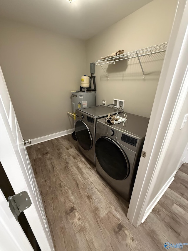 clothes washing area with water heater, washer and clothes dryer, and wood-type flooring