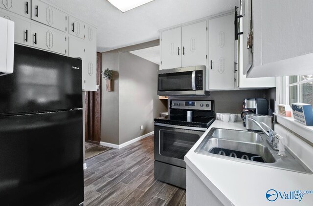 kitchen with white cabinetry, a sink, stainless steel appliances, baseboards, and dark wood-style floors