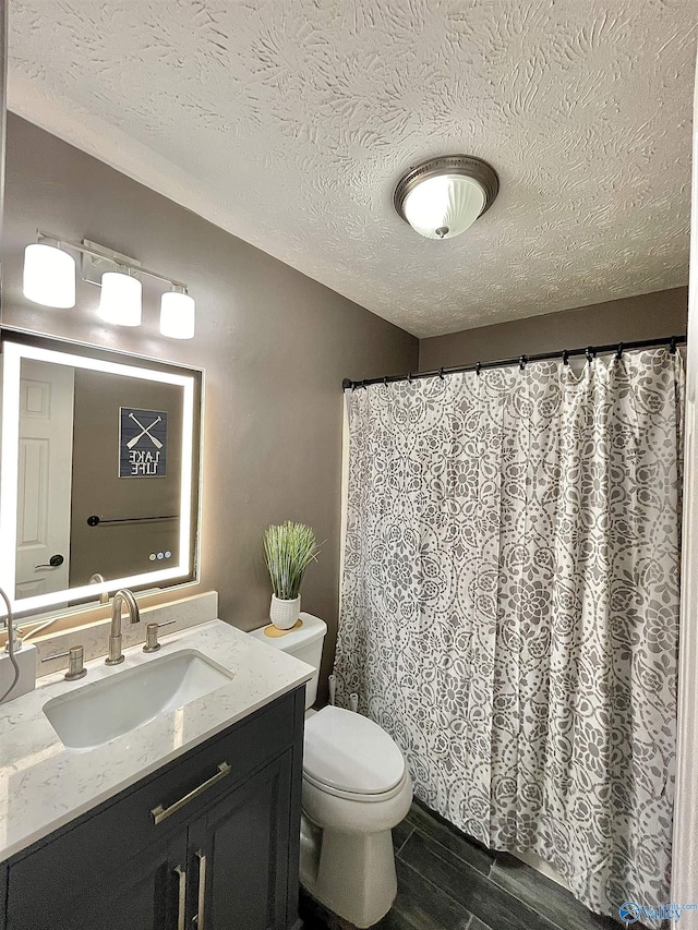 full bathroom featuring toilet, vanity, wood finished floors, and a textured ceiling
