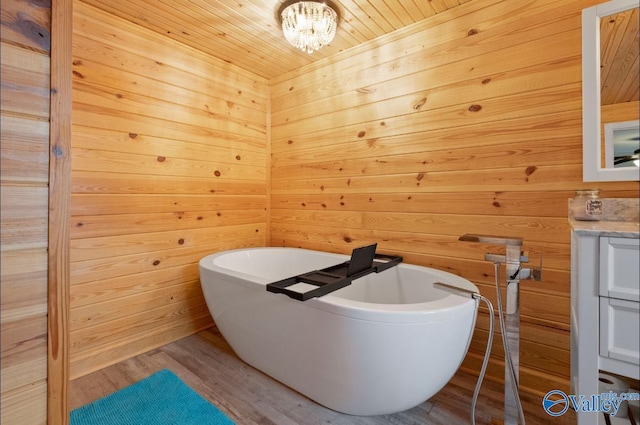 bathroom featuring a freestanding tub, vanity, an inviting chandelier, wooden walls, and wood finished floors