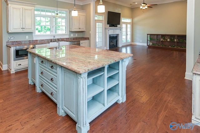 kitchen featuring dark wood-type flooring, appliances with stainless steel finishes, light stone countertops, a center island with sink, and decorative light fixtures