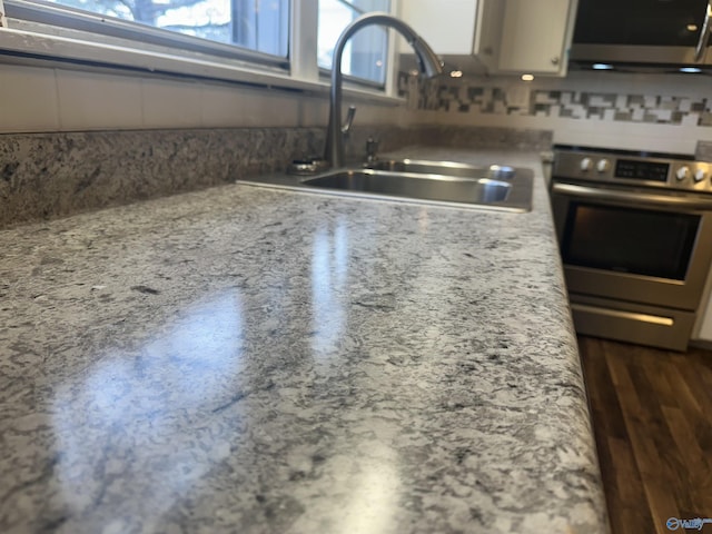 kitchen featuring light stone countertops, range, tasteful backsplash, and sink