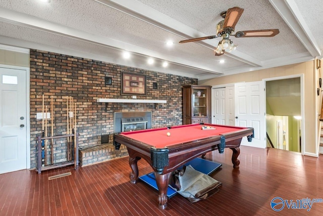 game room with pool table, hardwood / wood-style flooring, beamed ceiling, a brick fireplace, and a textured ceiling