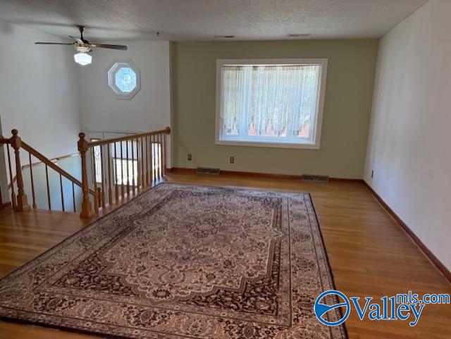 unfurnished living room featuring visible vents, a textured ceiling, baseboards, and wood finished floors