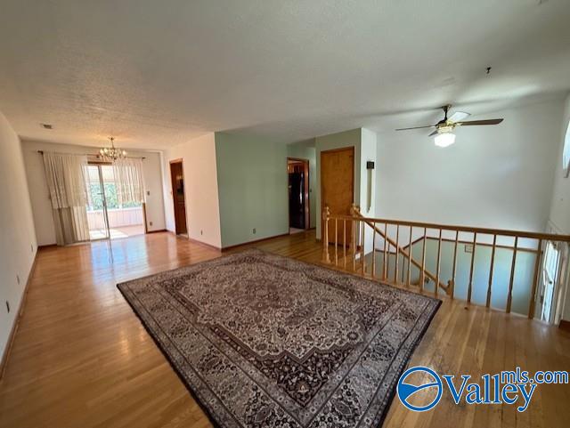 spare room with ceiling fan with notable chandelier, wood finished floors, and baseboards