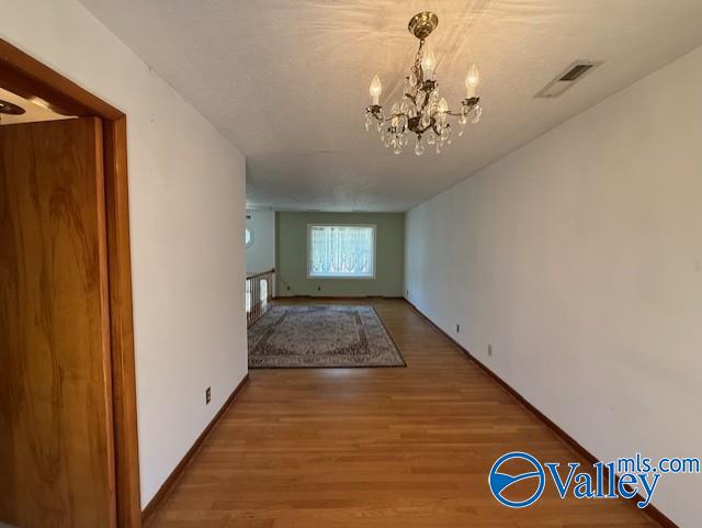 corridor with baseboards, visible vents, a chandelier, and wood finished floors