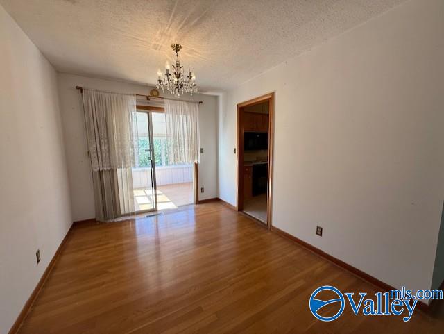 unfurnished room with a notable chandelier, a textured ceiling, baseboards, and wood finished floors