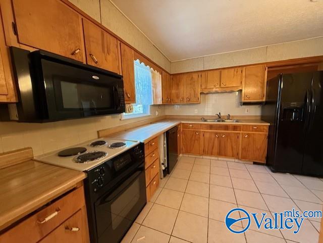 kitchen featuring light tile patterned floors, a sink, light countertops, brown cabinets, and black appliances