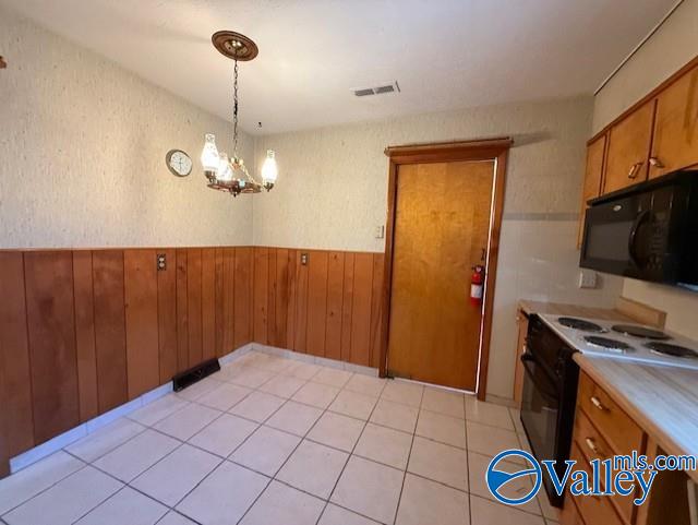 kitchen with visible vents, a wainscoted wall, brown cabinets, black appliances, and a notable chandelier