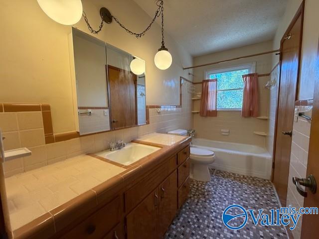 full bathroom featuring a textured ceiling, toilet, vanity, tile walls, and tub / shower combination