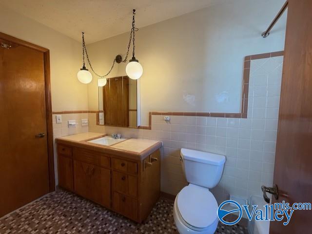 bathroom with toilet, a wainscoted wall, vanity, and tile walls