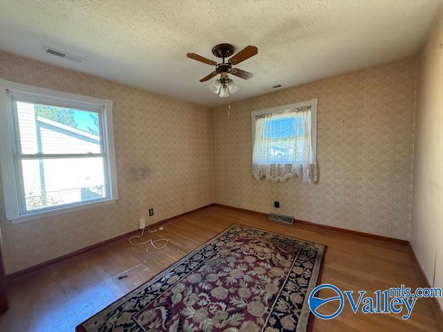 spare room with wood finished floors, visible vents, and wallpapered walls