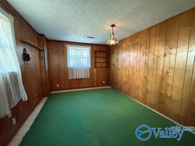 carpeted empty room featuring wooden walls, visible vents, and a textured ceiling