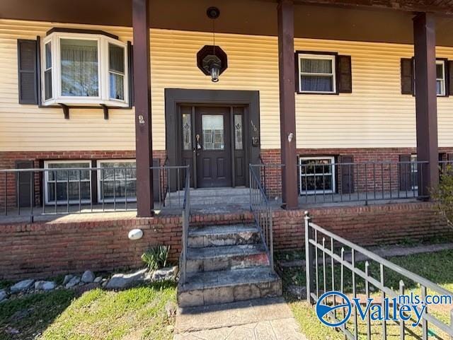 view of exterior entry featuring covered porch and brick siding