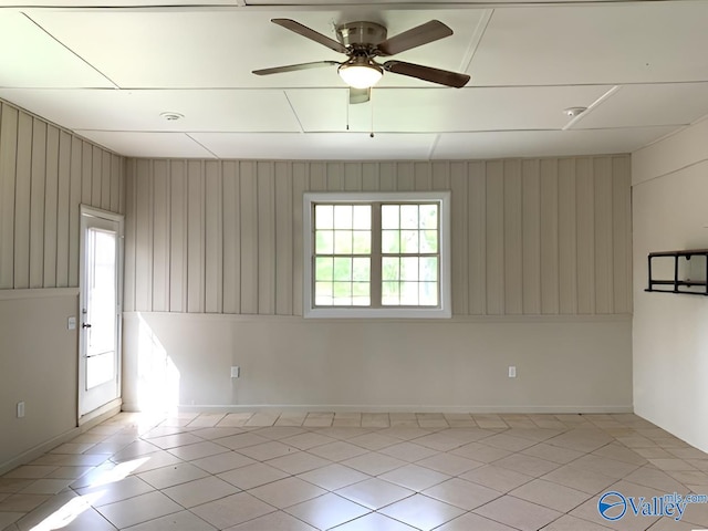 tiled empty room with ceiling fan and wood walls