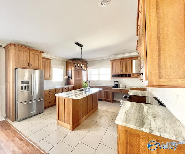 kitchen featuring a center island with sink, high quality fridge, hanging light fixtures, light stone countertops, and ornamental molding