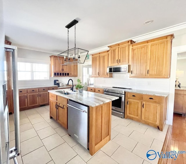 kitchen featuring a center island with sink, sink, hanging light fixtures, ornamental molding, and stainless steel appliances