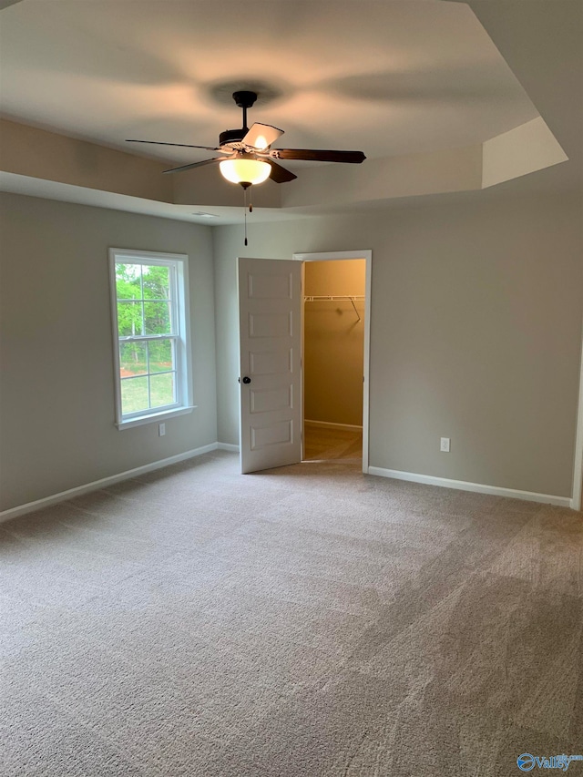 unfurnished bedroom featuring a closet, carpet flooring, ceiling fan, and a walk in closet