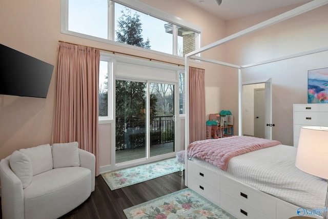 bedroom featuring dark wood-style flooring, access to exterior, and a towering ceiling