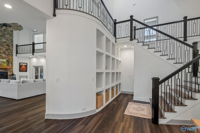 staircase with a stone fireplace, baseboards, a towering ceiling, and wood finished floors