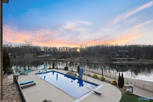 pool at dusk with a patio, a fenced in pool, a water slide, a diving board, and a water view