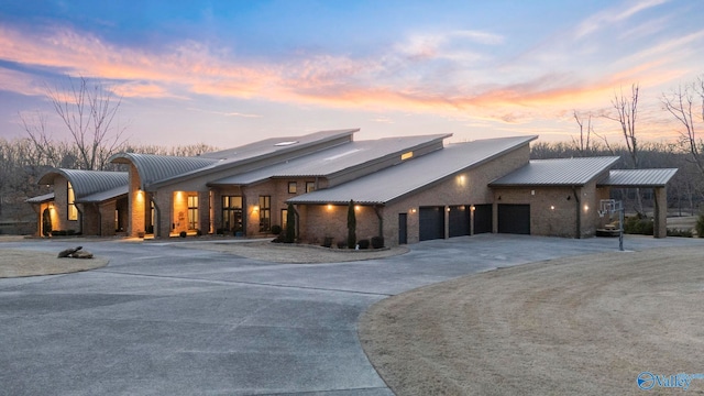 view of front of property featuring a standing seam roof, stone siding, curved driveway, an attached garage, and metal roof