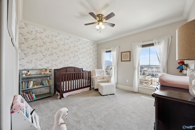 carpeted bedroom with ornamental molding, a nursery area, and ceiling fan