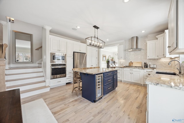 kitchen featuring wall chimney range hood, sink, appliances with stainless steel finishes, white cabinetry, and a center island