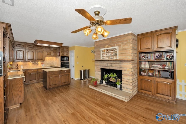 kitchen with a brick fireplace, a center island, hardwood / wood-style floors, and black appliances