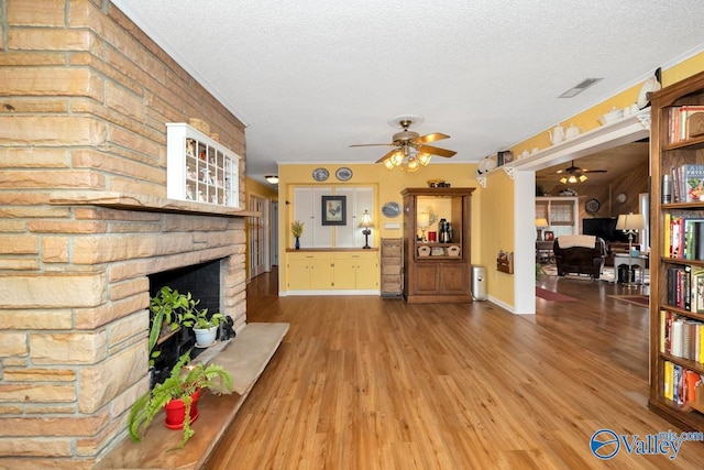 living room featuring ceiling fan, hardwood / wood-style flooring, a fireplace, and a textured ceiling