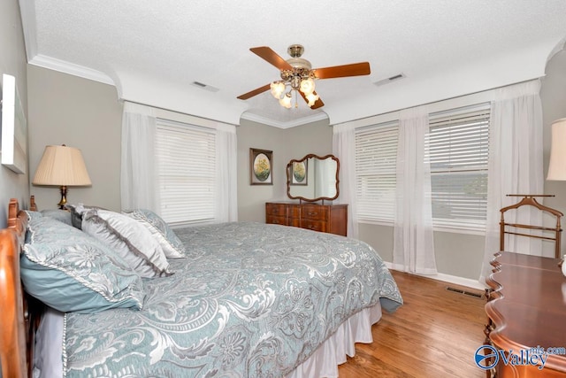 bedroom featuring ceiling fan, ornamental molding, light hardwood / wood-style floors, and a textured ceiling