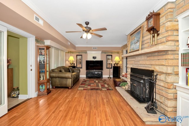 living room with crown molding, light hardwood / wood-style floors, ceiling fan, and a wood stove